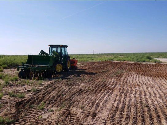 A large green tractor next to an open dirt field with clean dirt lines.